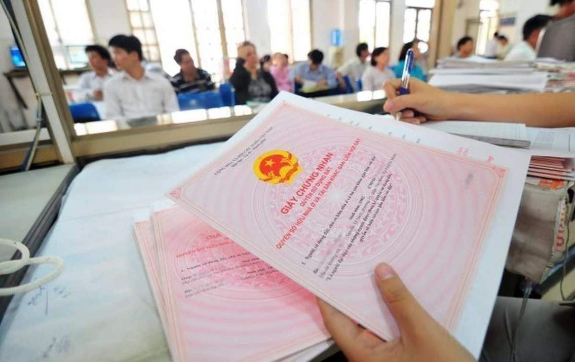 giải quyết thủ tục liên quan đến nhà sổ hồng chung trong văn phòng đăng ký đất đai, một người đang cầm cuốn sổ hồng