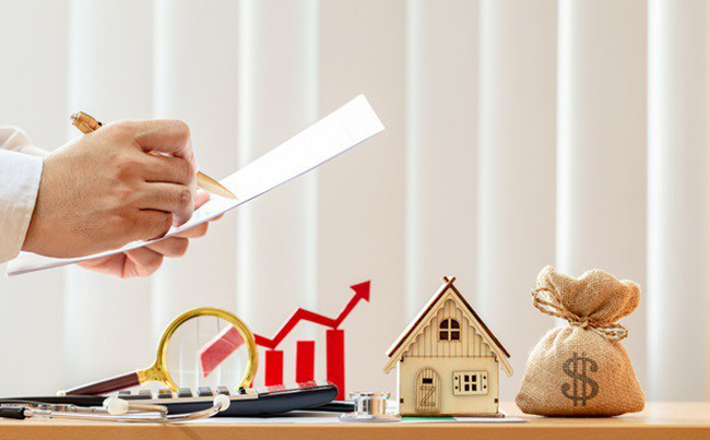vay thế chấp ngân hàng một người đang cầm tờ giấy tính toán các con số, trên bàn có mô hình ngôi nhà