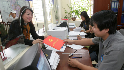 sang tên sổ đỏ là thủ tục bắt buộc khi chuyển nhượng nhà đất. hình ảnh trong văn phòng đăng ký đất đai, 2 người đang trao và nhận cuốn sổ đỏ