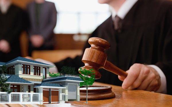 một người đang ngồi cầm búa thẩm phán, bên cạnh là hình ảnh ngôi nhà